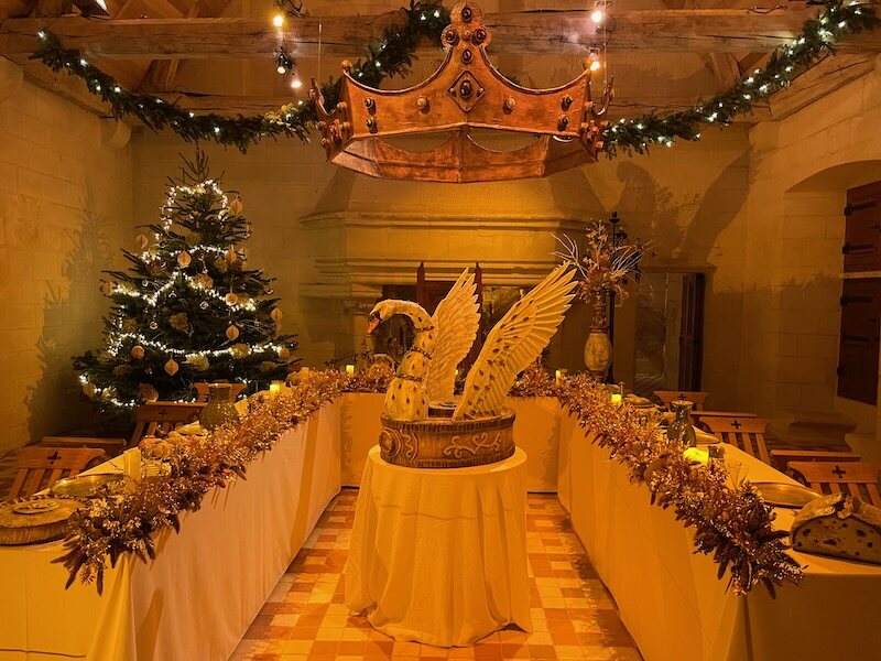 A loaded banquet table, with a crown hanging from the ceiling and a dressed bird in a dish at Chinon Fortress