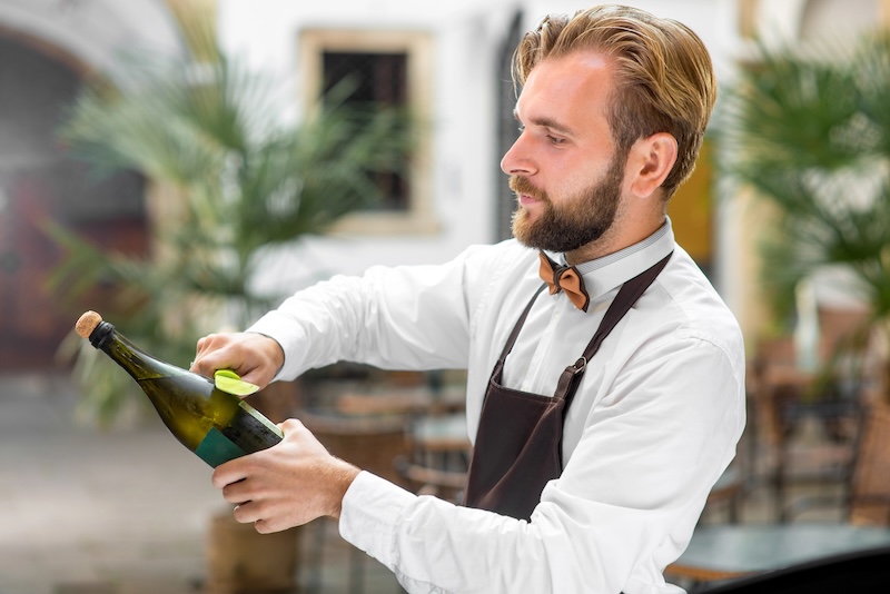 A young man uses a saber to pop open a bottle of champagne, a technique known as Sabrage